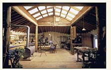 Interior of shop (looking through doors shown above). Structure was inspired by the painting of a Mandan earth lodge in Shelter (at right). This is a classic framing structure, with interior posts and beams providing mid-way support for rafters that span from lower exterior walls. Skylight has two layers of fiberglass: corrugated on outside, flat fiberglas on inside so there's an air space and good insulation.