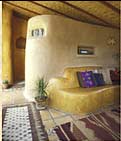 Interior of guest cottage, by-product of first straw bale workshop/happening in 1990. Adobe wall/seat divides bathroom space from living area. Back side of the wall forms lime-plastered shower.